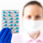 Mulher com uma luva médica de borracha azul segura uma cartela de importadora de medicamentos